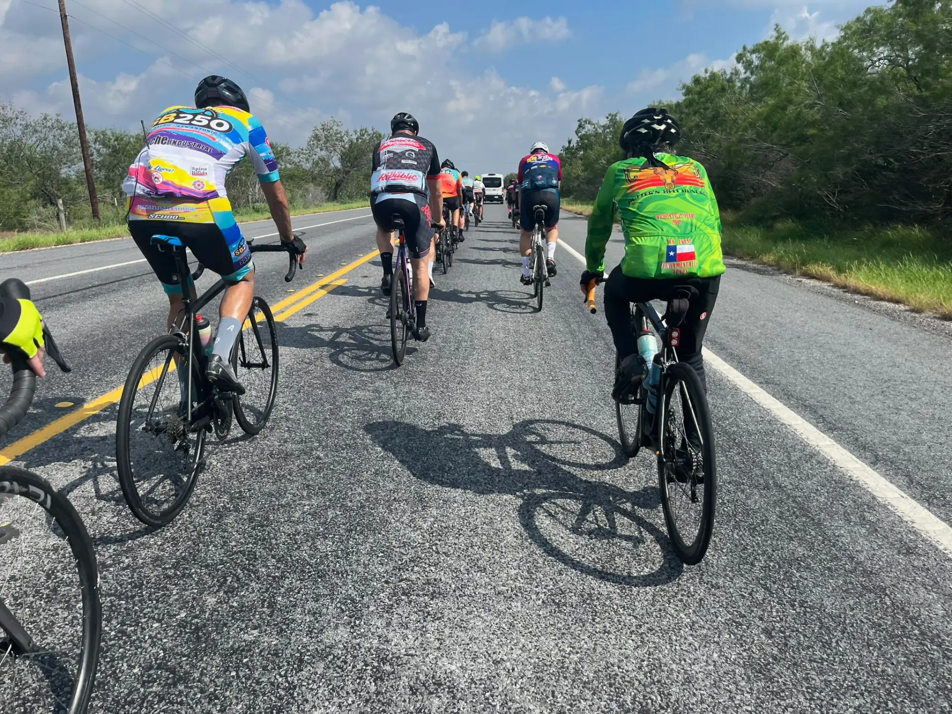 Group of cyclists riding together on a paved road under a wide sky